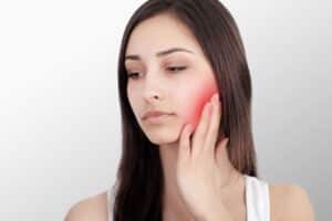 Close-up portrait of a woman holding her cheek in pain with a red highlight indicating a severe toothache